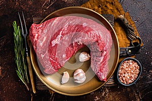 Raw tri-tip triangle roast or bottom sirloin steak on plate with herbs. Dark background. Top view