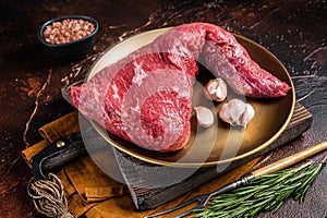 Raw tri-tip triangle roast or bottom sirloin steak on plate with herbs. Dark background. Top view