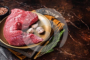 Raw tri-tip triangle roast or bottom sirloin steak on plate with herbs. Dark background. Top view. Copy space