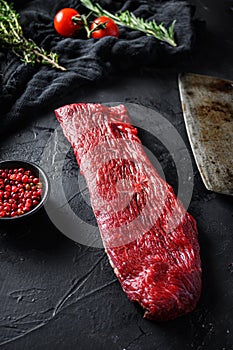 Raw triangle roast or tri tip, near butcher knife with pink pepper and rosemary. Black background. Close up side view selective