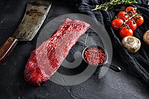 Raw triangle  roast or tri tip, near butcher knife with pink pepper and rosemary. Black background. side view