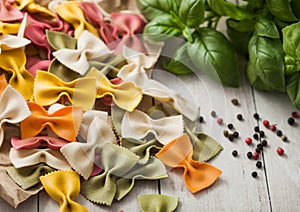 Raw tricolore farfalle pasta in brown paper on light wooden background with basil and garlic