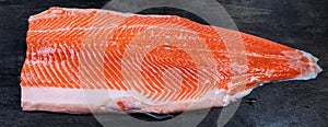 Raw trout fillet on the skin on a dark surface