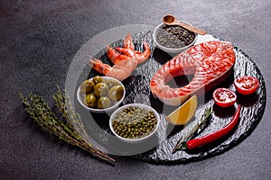 Raw trout red fish steak served with herbs and lemon and olive oil on a dark background