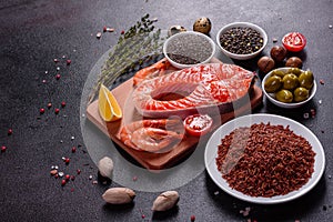 Raw trout red fish steak served with herbs and lemon and olive oil on a dark background