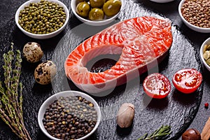 Raw trout red fish steak served with herbs and lemon and olive oil on a dark background