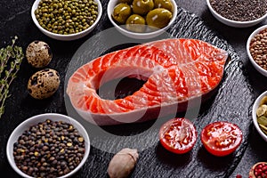 Raw trout red fish steak served with herbs and lemon and olive oil on a dark background