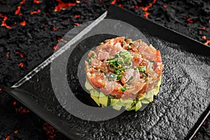 Raw tuna, avocado onion salad served in culinary ring on black plate. Black  background. Tartar