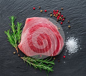 Raw tuna fish steak on natural stone black slate serving plate. Top view