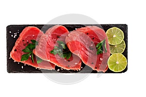 Raw tuna steak with lemon and herbs on black slate cutboard