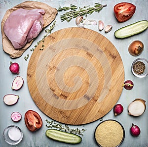 Raw turkey breast with tomato and pepper radish herbs and cucumbers over wooden cutting board on rustic wooden background top view