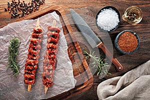 Raw Turkish Adana kebab on white cooking paper and wooden cutting table. Dercorated with herbs, spices and chef`s knife