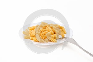 Raw uncoocked pasta fusilli in white ceramic plate with a folk isolated on white, italian cousine concept