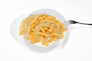 Raw uncoocked pasta fusilli in white ceramic plate with a folk isolated on white, italian cousine concept