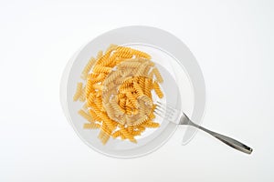 Raw uncoocked pasta fusilli in white ceramic plate with a folk isolated on white, italian cousine concept