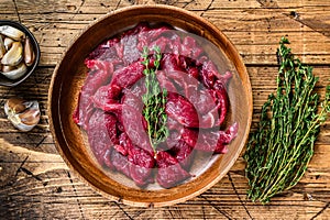 Raw uncooked beef meat sliced in strips with fresh herbs for beef stroganoff. wooden background. Top view