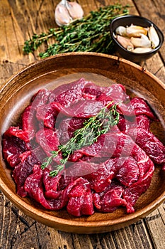 Raw uncooked beef meat sliced in strips with fresh herbs for beef stroganoff. wooden background. Top view