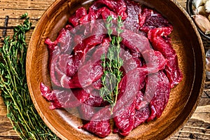 Raw uncooked beef meat sliced in strips with fresh herbs for beef stroganoff. wooden background. Top view