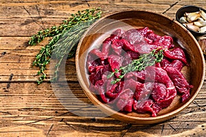 Raw uncooked beef meat sliced in strips with fresh herbs for beef stroganoff. wooden background. Top view. Copy space