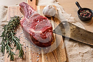 Raw uncooked black angus beef dry steak cowboy on chopping board with herbs and spices and butcher knife