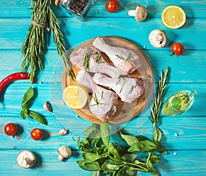Raw uncooked chicken legs, drumsticks on blue wood background, meat with ingredients for cooking.