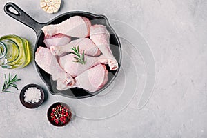 Raw uncooked chicken legs with rosemary and spices in cast iron pan