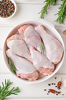 Raw uncooked chicken legs in a white dish on a white wooden background. Meat with ingredients for cooking. Top view