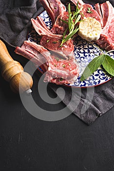 Raw uncooked lamb chops with herbs and spices on bright plate over dark wooden background, copy space