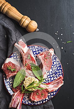 Raw uncooked lamb chops with herbs and spices on colorful plate over dark wooden background