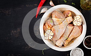 Raw uncooked marinated chicken legs, drumsticks for cooking on dark table.