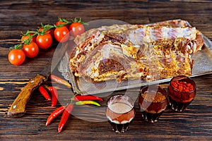 Raw uncooked rack of lamb on wooden chopping board with salt, pepper and dry herbs over old wood background