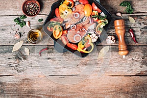 Raw uncooked salmon fish with vegetables, herbs, spices in iron grilling pan over wooden background. Top view, copy space. Healthy