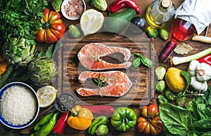 Raw uncooked salmon fish with vegetables, rice, herbs, spices and wine on chopping board over rustic wooden background