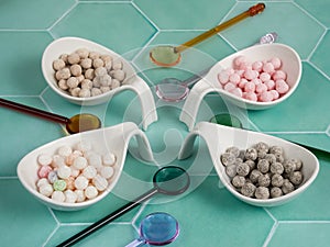 Raw, uncooked tapioca balls with different flavors (boba for bubble tea), on green tile background.