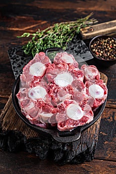 Raw veal beef Oxtail Meat on butcher wooden board with cleaver. Dark wooden background. Top view