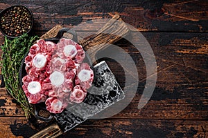 Raw veal beef Oxtail Meat on butcher wooden board with cleaver. Dark wooden background. Top view. Copy space