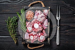 Raw veal beef Oxtail Meat in wooden tray with thyme. Black wooden background. Top view