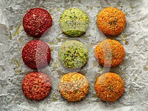 Raw vegan burgers made of beetroot, green peas, carrots, groats and herbs on white parchment prepared for baking, top view.