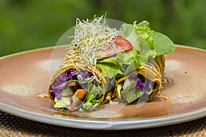 Raw vegan carrot and cumin wrap roll stuffed with shred lettuce, tomato, avocado, spinach and savory zucchini hummus