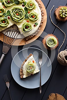 Raw vegan dessert. Homemade pie with kiwi roses, berries and cream filling on nutty crust on dark background