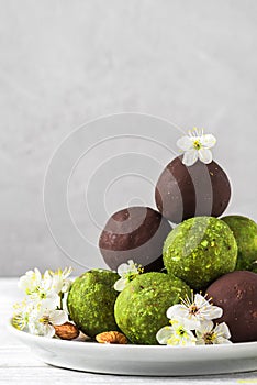 Raw vegan energy balls made of matcha tea, dates and nuts and balls in chocolate glaze with spring blossom flowers