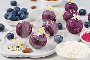 Raw vegan energy bites or balls made of blueberry, acai, nuts and dates served with flowers. Food styling