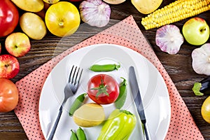 Raw vegan food concept. Raw vegetables, plate with cutlery and napkin on wooden background