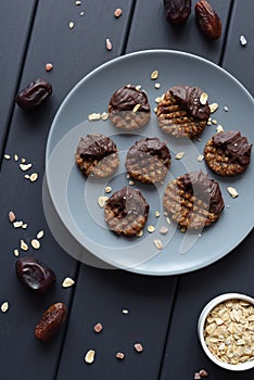 Raw vegan gluten free cookies with chocolate glaze served with ingredients: oats, dates and himalayan salt on grey plate