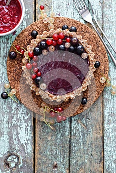 Raw vegan pie with berry jam and organic currants on blue background copyspace