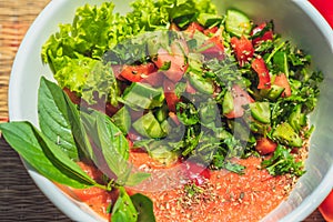 Raw vegan salad with green leaves mix vegetables in white bowl. Cooking recipe blended tomato carrot, parsley cilantro