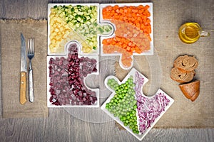 Vegan salad in the form of jigsaw puzzles from plates with different vegetables. Raw vegetables carrots, peas, onions, cucumber, p