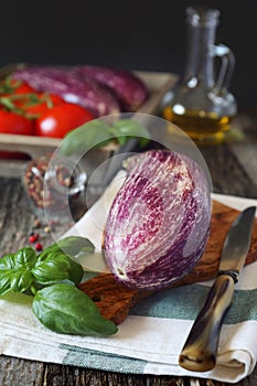 Raw vegetables: graffiti eggplants, tomatoes in tray, and olive oil and basil