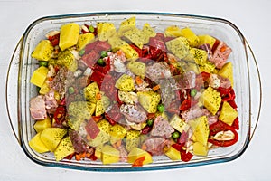 Raw vegetables  potatoes, carrots, green peas, red pepper and onion with pork meat garlic and spices in pyrex tray prepared for