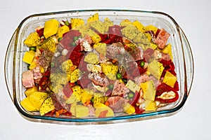 Raw vegetables  potatoes, carrots, green peas, red pepper and onion with pork meat garlic and spices in pyrex tray prepared for